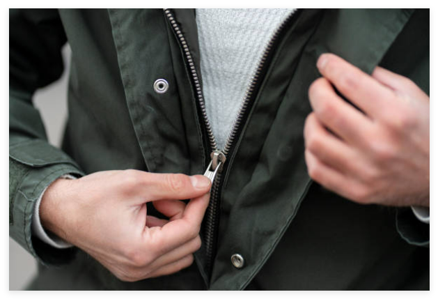 Close-up of a person zipping up a green jacket, showing the zipper mechanism and hands adjusting it