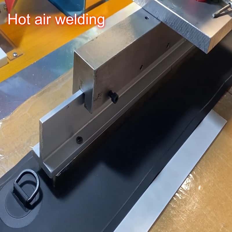 Industrial hot air welding machine setup with metal clamping fixtures securing a black thermoplastic sheet for seamless plastic joint fabrication