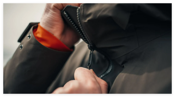 A person zipping up a dark - colored outdoor jacket, highlighting the zipper's functionality