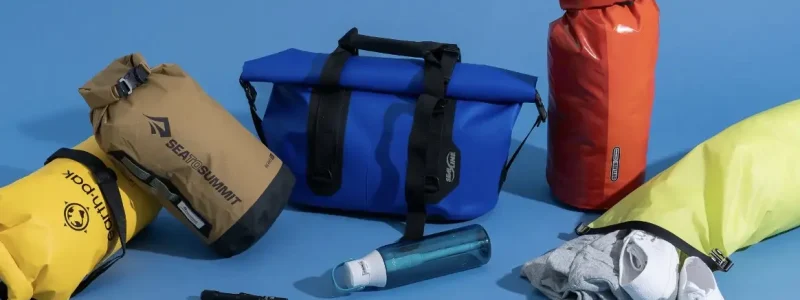 A collection of colorful waterproof bags and pouches, including brands like Sea to Summit, along with a flashlight, water bottle, and clothes, set against a blue background